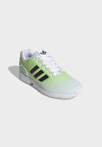 Green and white athletic shoe featuring a mesh upper, black three-stripe design, and a textured rubber sole for grip.