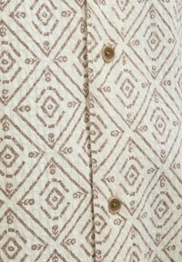 Leinenhemd mit einem cremefarbenen Hintergrund und einem braunen Diamantmuster, detaillierter Textur und einem runden braunen Knopfverschluss vorne.