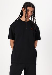 Black short-sleeve T-shirt made of cotton, featuring a small red and yellow logo on the left chest and a loose, relaxed fit.