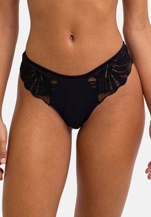 Sous-vêtement bikini en dentelle noire porté par une femme, avec des panneaux en dentelle florale transparente sur les côtés et un panneau avant en tissu uni.