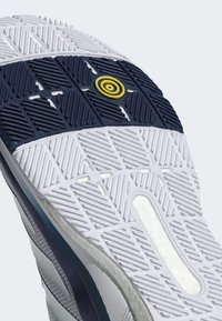 Σολα αθλητικού παπουτσιού με λευκό και ναυτικό σχέδιο από καουτσούκ. Διαθέτει υφές και έναν κυκλικό κίτρινο τονισμό στο κέντρο.