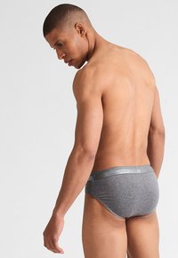 Slip in cotone grigio con una texture liscia, dotato di una vita elastica metallica. Il design è aderente con una copertura minima sul retro.