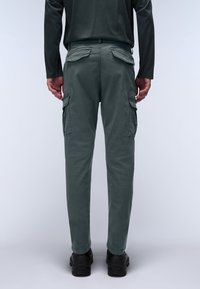 Harmaat työhaalarit, rento istuvuus, joissa sivutaskut ja sileä pinta. Päällä mustat kengät, kuva takaa päin.