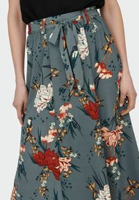 Blomstre midi-nederdel i dæmpet teal-stof, med røde og cremefarvede blomster, grønne blade, plisseret design og taljebånd.