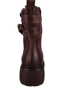 Brązowy skórzany botek za kostkę z wieloma dekoracyjnymi paskami, zaokrąglonym noskiem i masywnym obcasem. Teksturowana cholewka z widocznym przeszyciem.