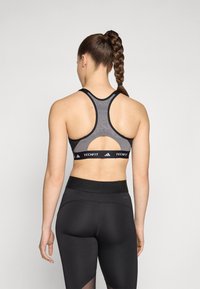 Black sports bra with mesh detailing and a cut-out back, featuring a branded elastic band. Black high-waisted leggings with subtle seams.