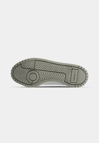 Suela de zapatilla blanca con una textura de goma ondulada, que presenta un acento circular y surcos finos. La marca es visible en el lateral.