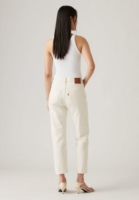 Witte tanktop gecombineerd met lichtbeige rechte jeans met een rafelende zoom en een bruine leren patch op de achterzijde van de tailleband.