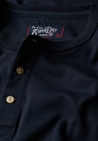 Marineblå, bomulds polo skjorte med rund halsudskæring, tre knapper og et mærket label. Blød tekstur med minimal krølning.