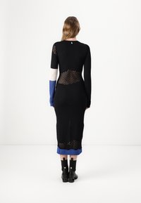 Svart stickad klänning med öppna mesh-sektioner. Har långa ärmar i vitt och blått, ribbade manschetter och en blå nederkant. Svarta anklarstövlar ingår.