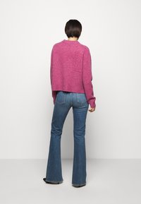 Fuchsia kortärmad tröja med rund hals, i ullblandning; kombinerad med utsvängda blå jeans och svarta skor, sedd bakifrån.