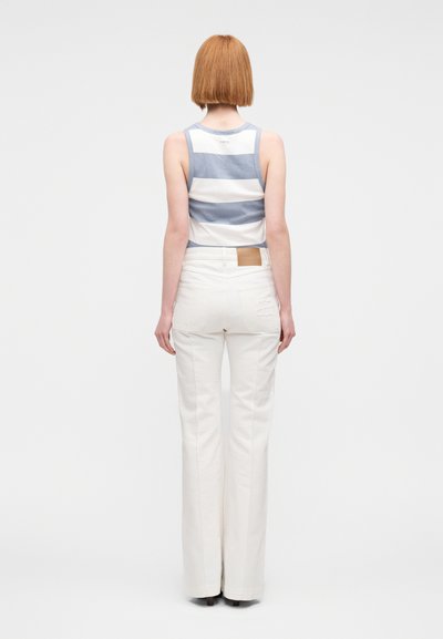 Αμάνικο ριγέ τοπ σε μπλε και λευκό, συνδυασμένο με ψηλόμεσα, εκρού φλογερά τζιν παντελόνια με δερμάτινο πίσω λάστιχο και ραφές λεπτομέρειες.