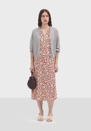 Cardigan grigio chiaro sopra un abito maxi floreale con motivi rossi e beige. Una borsa rotonda scura e sandali beige completano l'outfit.
