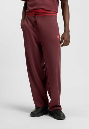 Maroon sweatpants with a contrasting red drawstring and waistband. Features side pockets and a small logo on the left leg. Smooth texture.