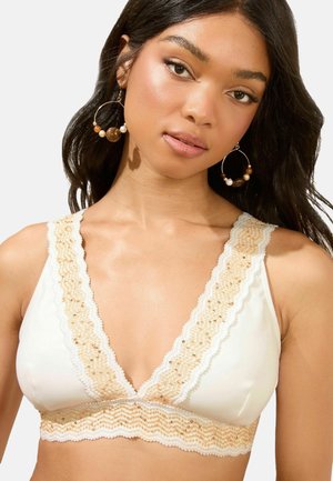 Witte bralette met een diepe V-halslijn, voorzien van een scalloped kant trim in beige en gouden kralen langs de randen. Gladde stof en zachte textuur.