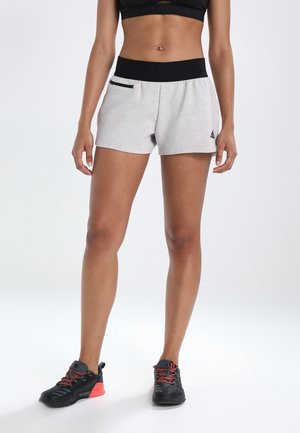 Kvinde iført lysegrå atletiske shorts med sort linning og sort- og pink sportssko, vist fra talje til fødder.