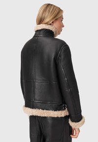 Svart läderjacka med en fluffig beige krage och fåll, med en strukturerad passform, synliga sömmar och detalj med sidobuckla.