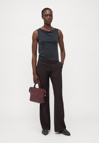 Černý top s kapucí spárovaný s hnědými kalhotami s vysokým pasem. Drží burgundskou kabelku. Šedé boty dokončují tento outfit.