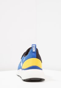 Nike tenisky v modré, černé a žluté barvě. Obsahují polstrovaný límec, bílý Swoosh logo a silnou bílou podrážku. Texturovaná tkanina a gumová podrážka.