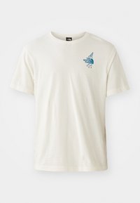 Lys kremfarget bomull t-skjorte med korte ermer, rund hals og en blå grafisk logo på venstre brystområde. Enkel design.