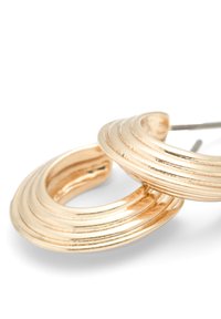 Guldtonade hoopörhängen med en lager-på-lager, vågig design. Strukturerad yta med växelvis polerade och matta ytor. Passar för hål i öronen.