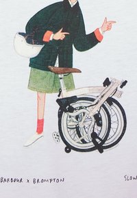 Osoba v zelené sukni a černé bundě drží helmu a ukazuje, zatímco stojí vedle složeného bílého kola.