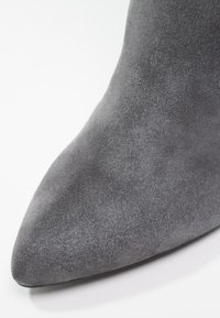 Botte en suède grise à bout pointu avec une texture lisse et une silhouette épurée, présentant un design à profil bas et sans matériel visible.