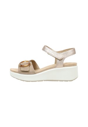 Sandalia cuña beige de ante y tira metálica con hebilla decorativa redonda en la tira delantera y suela gruesa blanca.