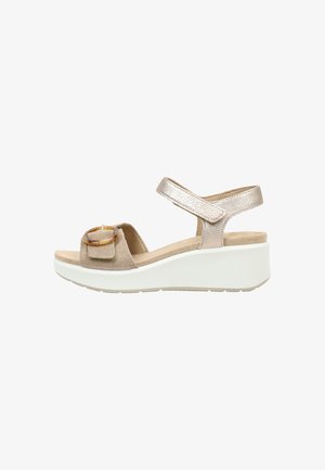 Sandalia cuña beige de ante y tira metálica con hebilla decorativa redonda en la tira delantera y suela gruesa blanca.
