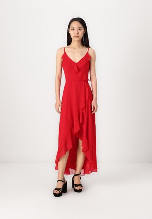 Red, sleeveless, long dress with a V-neck, ruffled detailing, asymmetrical hem, and a flowy silhouette. Paired with black platform sandals.