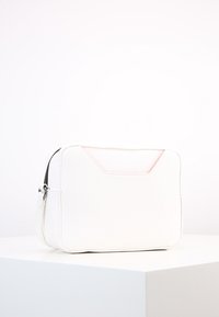 Liten rektangulär vit läderväska med svart dragkedja och en rosa texturerad detalj på en enkel vit yta.