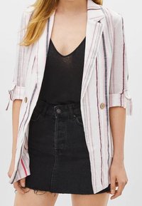 Randig kavaj i vitt, rosa och marinblått, med en enkel knappstängning, rullade ärmar och en avslappnad passform. Matchas med en svart kjol.