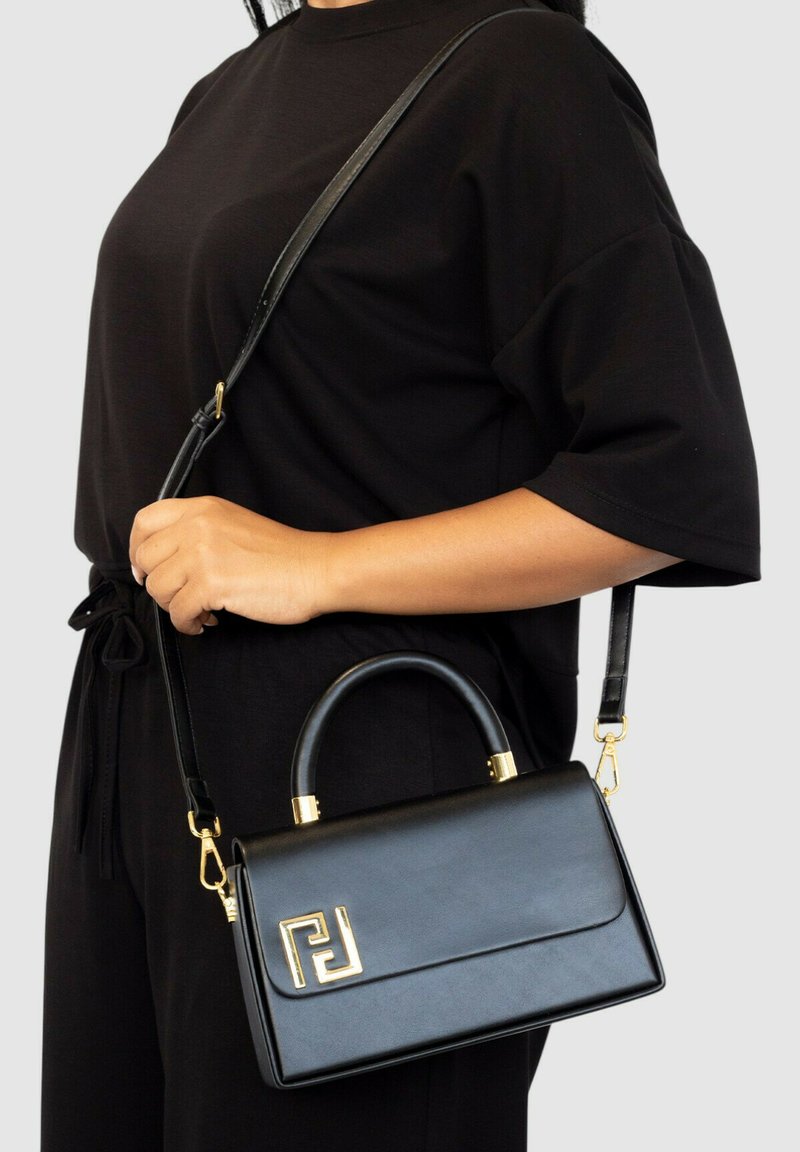 Bolso de mano de cuero negro con un diseño estructurado, acentos de hardware dorado, asas superiores y correa para el hombro desmontable, con un detalle de logo.