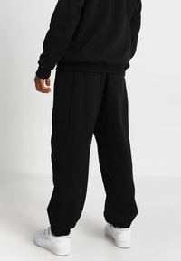 Pantalones de chándal negros con un ajuste relajado, que presentan puños elásticos y bolsillos laterales, combinados con zapatillas blancas para un look contrastante.