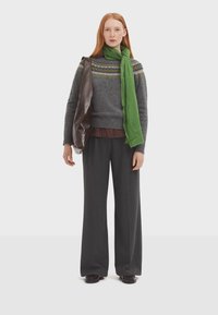 Pull en laine gris avec un motif multicolore, écharpe verte, sac à bandoulière marron, pantalon à bandage à rayures larges et chaussures noires.