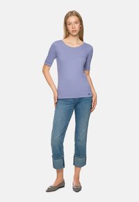 Helles lila Kurzarmoberteil mit runden Halsausschnitt, kombiniert mit cropped Jeans in Denim mit umgeschlagenen Säumen und grauen Ballerinas mit dekorativem Schnallenverschluss.