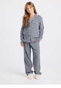 Ensemble de pyjama à carreaux bleu marine et blanc avec une chemise boutonnée dotée d'une poche et un pantalon ample assorti, accompagné de chaussons de couleur claire.