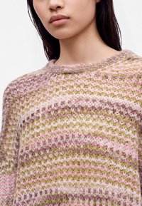 Gros plan d'une personne portant un pull tricoté avec des rayures horizontales roses, vertes et beiges, montrant l’encolure et le haut de la poitrine.