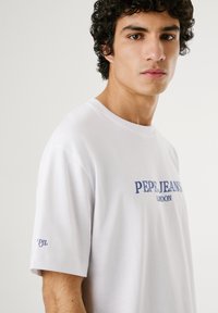 White cotton t-shirt with round neck, short sleeves, and blue "Pepe Jeans London" logo on the front and "PJL" text on the sleeve.