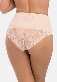 Beige spetsiga höga trosor med blommönster och scallopade kanter. Mjuk textur och halvgenomskinlig detalj på baksidan. Avslappnad passform.