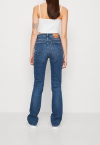 Fitted blue denim flared jeans with a mid-rise waist, five pockets, and a leather patch label on the back waistband.