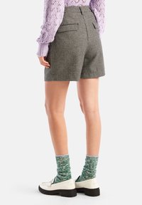 Högmidjade rutiga shorts i svart och vitt med bakfickor, tillsammans med gröna mönstrade strumpor och vita loafers.