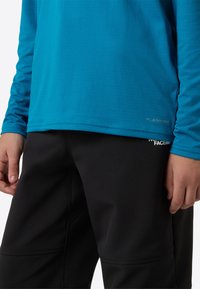 Modra srajca z dolgimi rokavi s teksturirano tkanino, kombinirana s črnimi hlačami. Na srajci je obrobni napis "FLASHDRY", hlače pa imajo šive in šivanje.