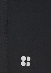 Tela negra con costuras visibles y un pequeño logotipo blanco compuesto por dos círculos y dos semicírculos en una disposición cuadrada.