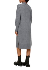Abito grigio a maglia con maniche lunghe e spacchi laterali, dotato di un orlo a coste. Abbinato a stivaletti neri alla caviglia. Design elegante e semplice.