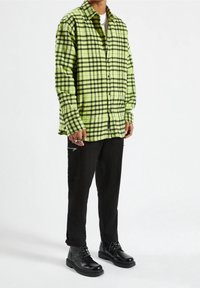 Groene en zwarte geruite flanellen overhemd, met knoopsluiting. Gecombineerd met zwarte broek met ritssluiting accenten en zwarte laarzen.
