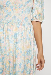 Vestido floral com corpete franzido em cores pastéis de azul, rosa e amarelo, com mangas bufantes e uma saia fluida.