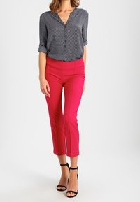 Blusa navy a pois con scollo a V e maniche arrotolate abbinata a pantaloni cropped rosa brillante. Il modello indossa scarpe con tacco nere a fasce.