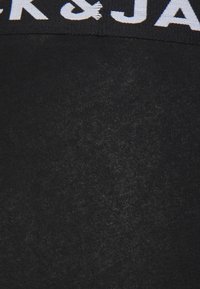 Tissu en coton noir avec une texture lisse, comportant une bande logo blanche contrastante au niveau de la taille. Design simple et minimal.