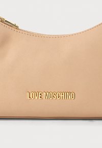Bēša ādas sajūgs soma ar zelta rāvējslēdzēju un zelta "LOVE MOSCHINO" uzrakstu centrā priekšpusē.